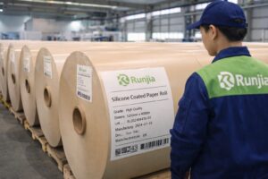 Runjia worker inspecting silicone coated paper jumbo rolls with traceability labels in warehouse
